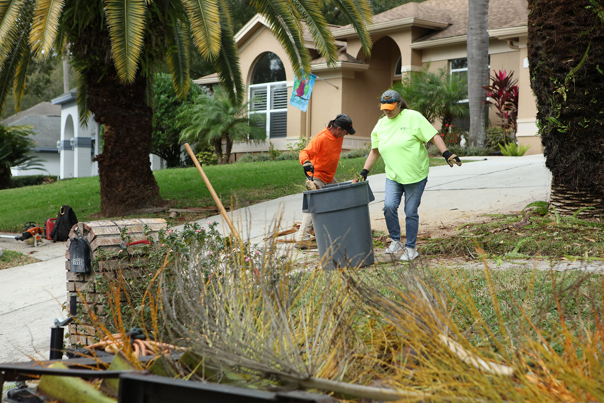 Man and woman filling trash can with yard trimmings in front of house.